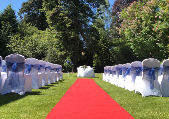 Outdoor ceremony set up with blue ribbons on chairs and red aisle walkway